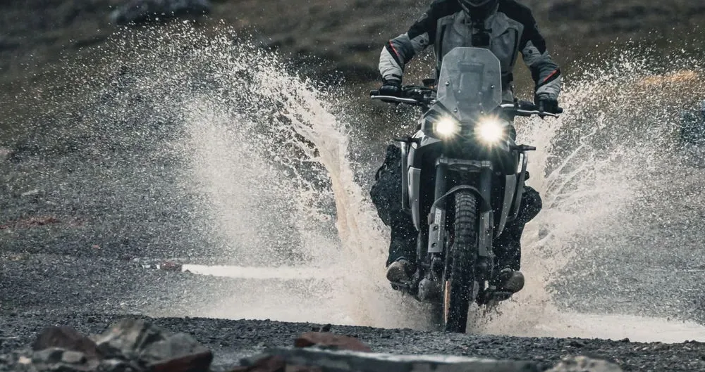 Une moto Kove 800 X Pro soulevant des gerbes d'eau en roulant dans une flaque d'eau