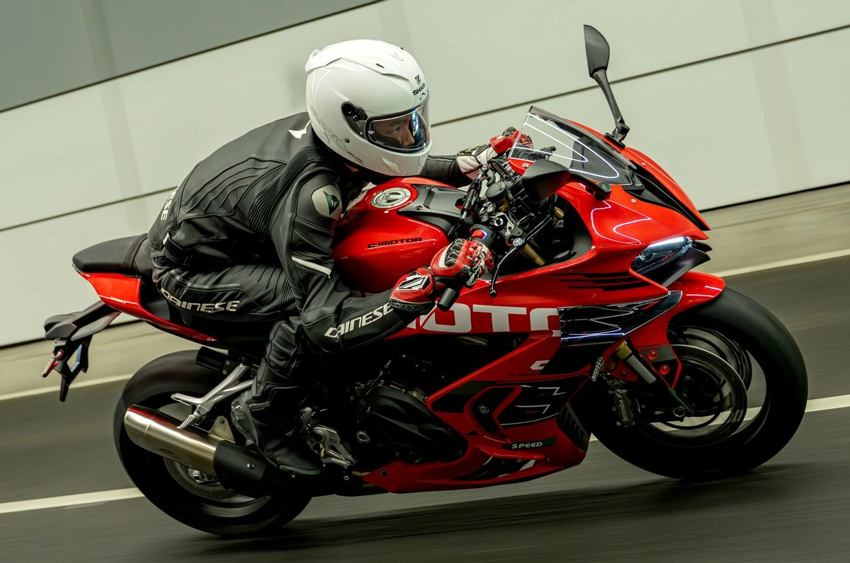Une moto QJ Motor SRK 800 RS rouge roulant dans un tunnel, un motard en combinaison noire Dainese avec un casque blanc.