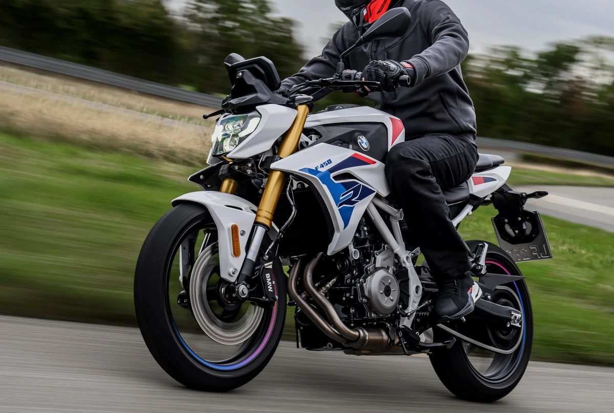 Une moto BMW F 450 R roulant sur route, un motard habillée en noir avec un casque rouge.