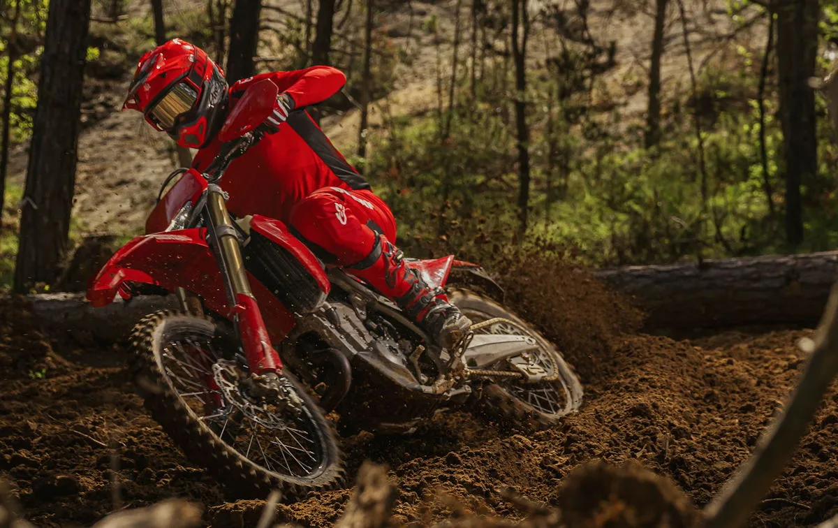Une Ducati Desmo450 EDS rouge en forêt et un pilote avec un casque et des vêtements rouges