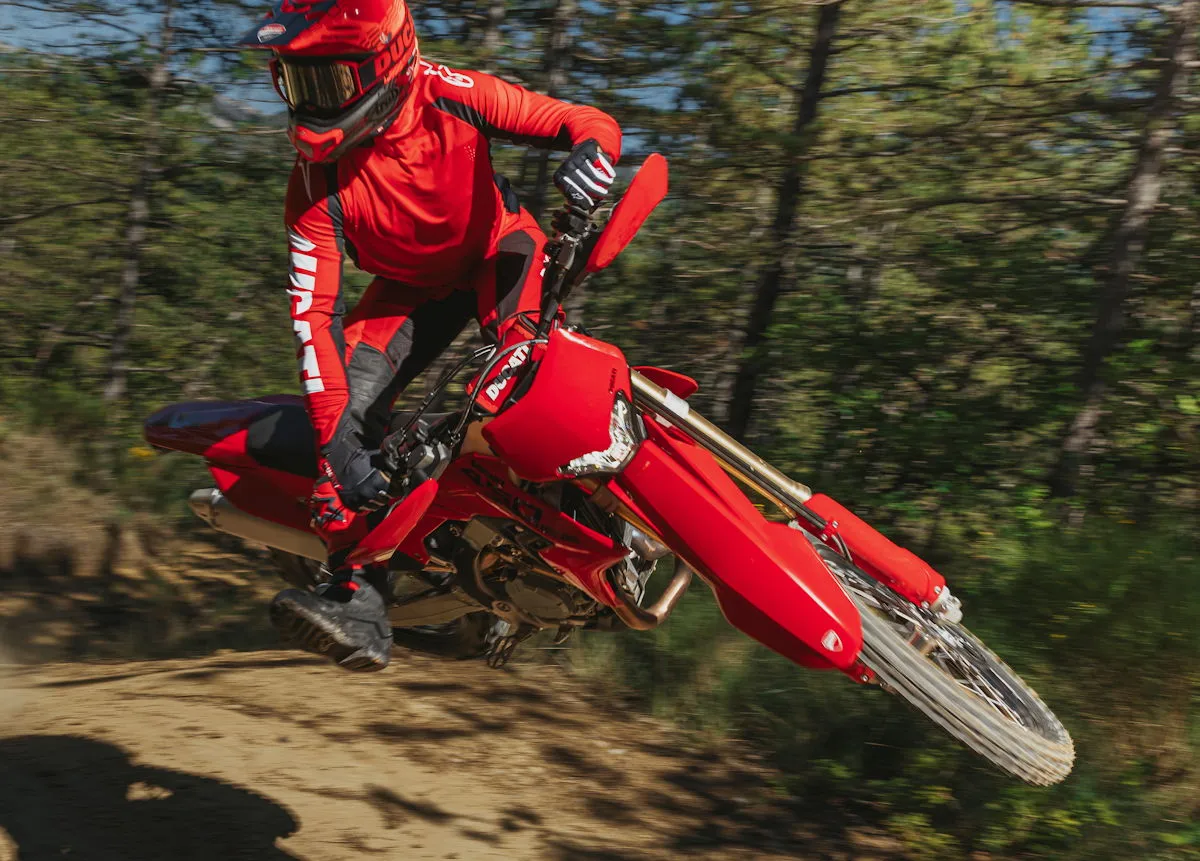 Une Ducati Desmo450 EDS rouge en forêt et un pilote avec un casque et des vêtements rouges
