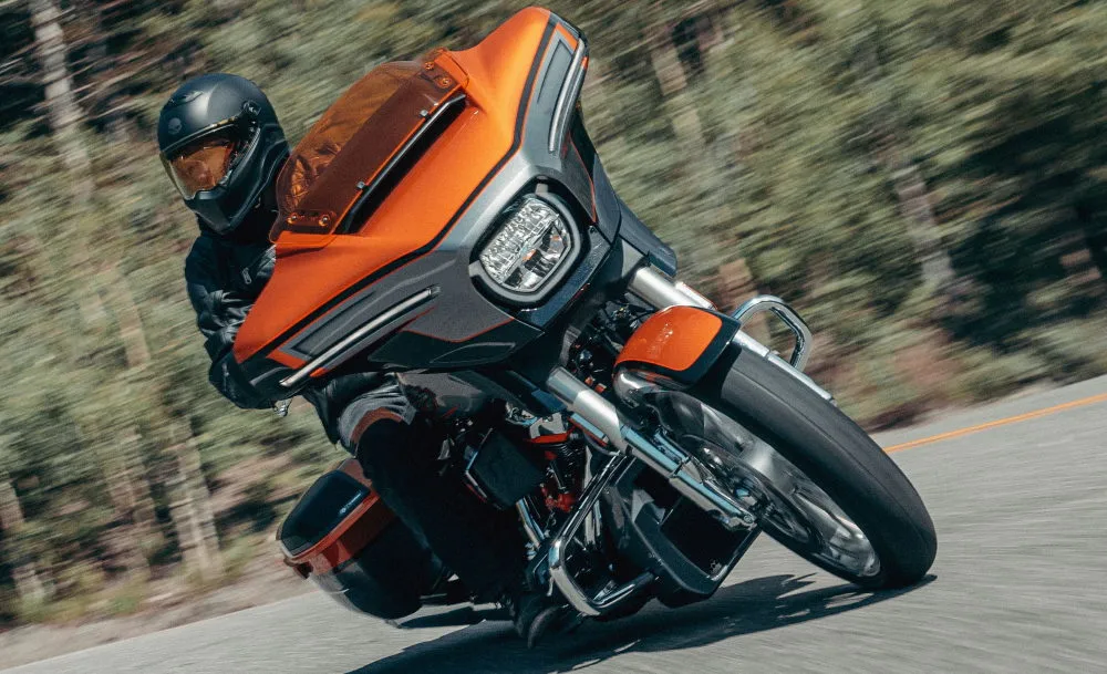 Une moto Harley-Davidson CVO 1980 Street Glide de 2026 orange sur la route et un motard avec un casque noir