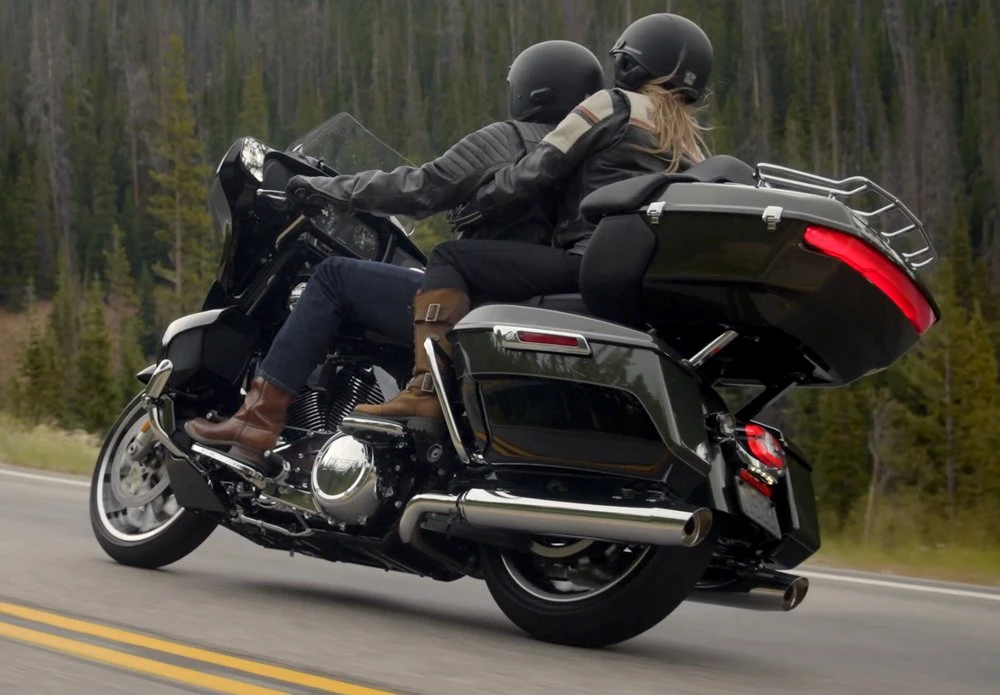 Une moto Harley-Davidson 1920 Street Glide Limited avec un couple de motard et une foret de conifères.