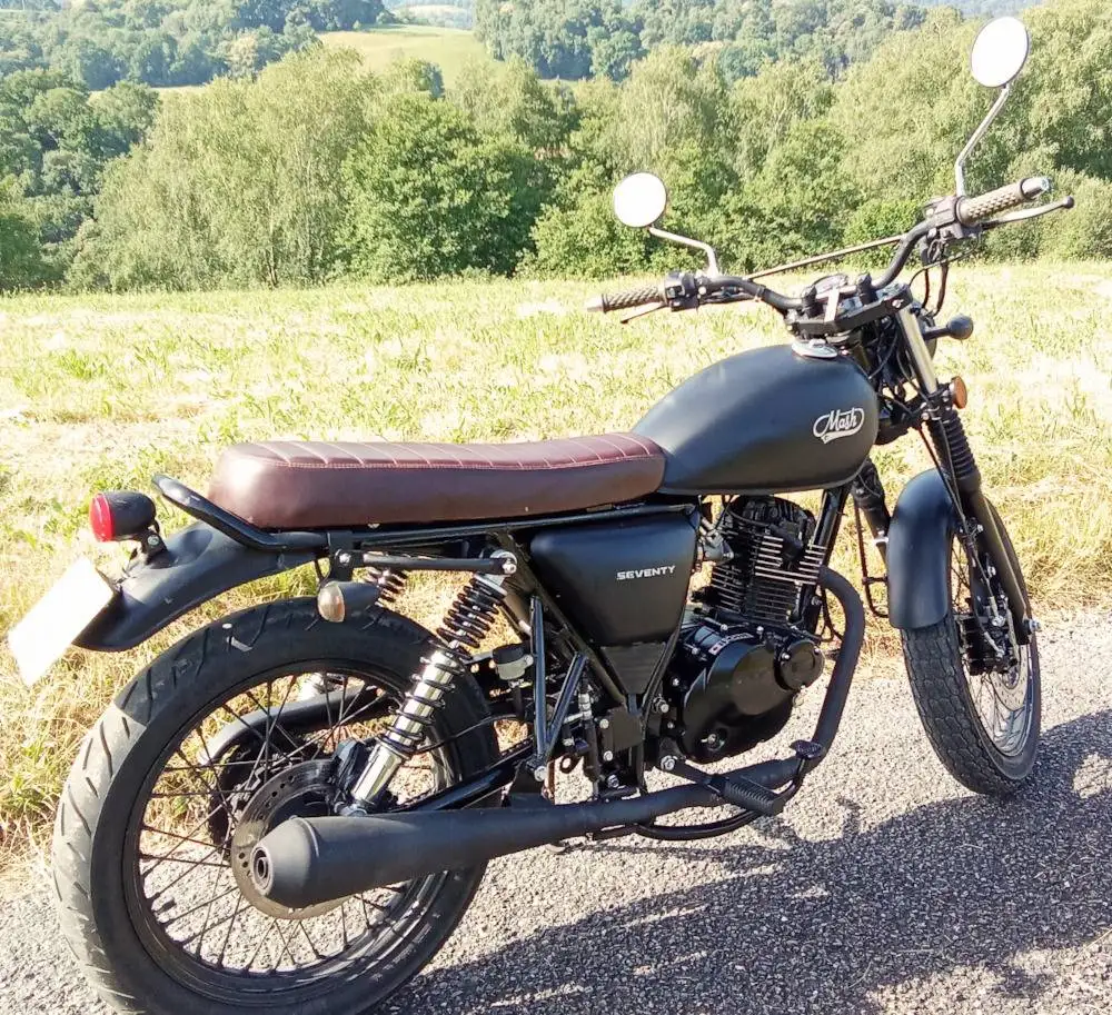 Une moto Mash 125 Seventy, un champ d'herbe et des arbres