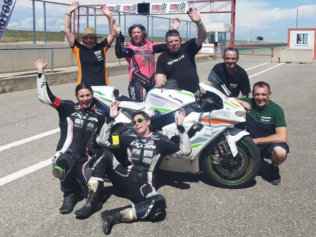 Plusieurs personnes autour d'une Kawasaki ZX-10R blanche, levant les bras, dans la ligne droite des stands d'un circuit moto.