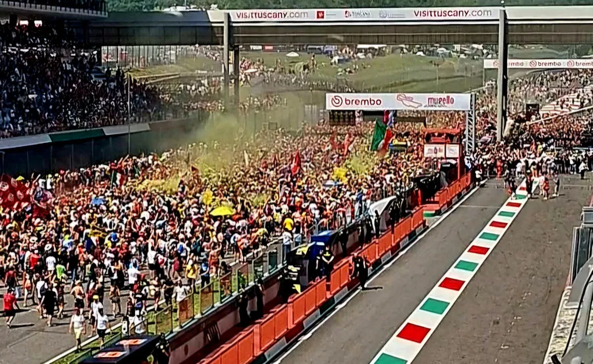 Du public envahissant la ligne droite du circuit du Mugello après une course et de la fumée jaune.