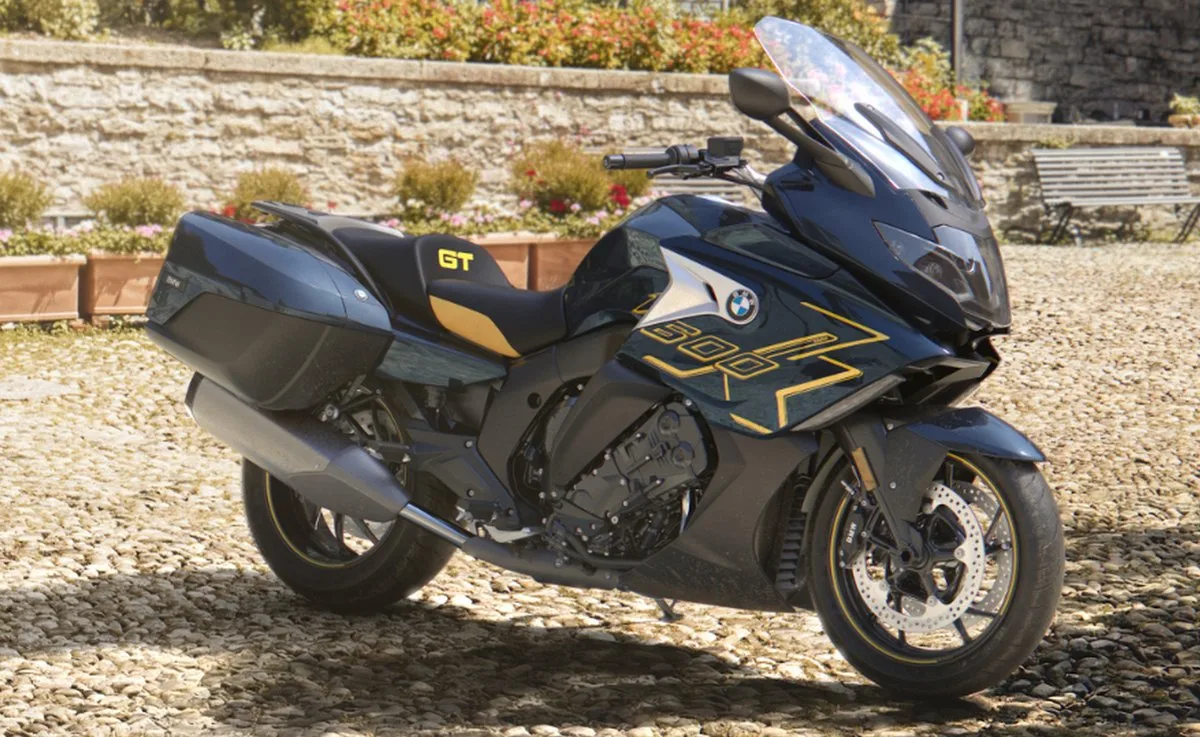 Une moto BMW K 1600 GT noire, avec des liserés jaunes, une allée en gravier et un mur en pierres