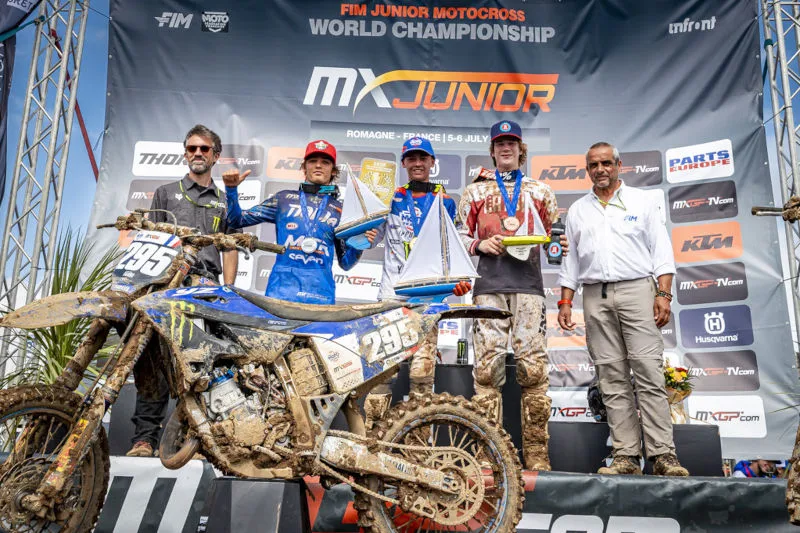 Podium MX Junior 2025 trois pilotes, les accompagnateurs, et la moto du vainqueur en premier pla