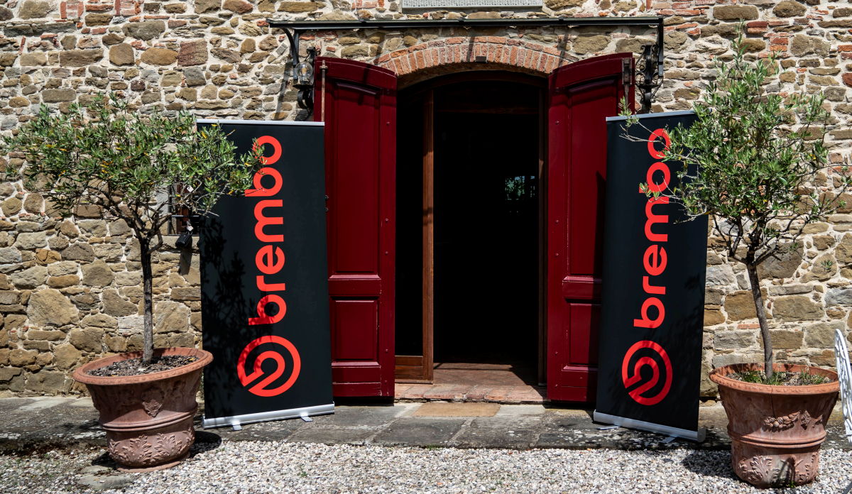 La puerta de entrada de una casa, dos árboles en maceta y dos pancartas de Brembo